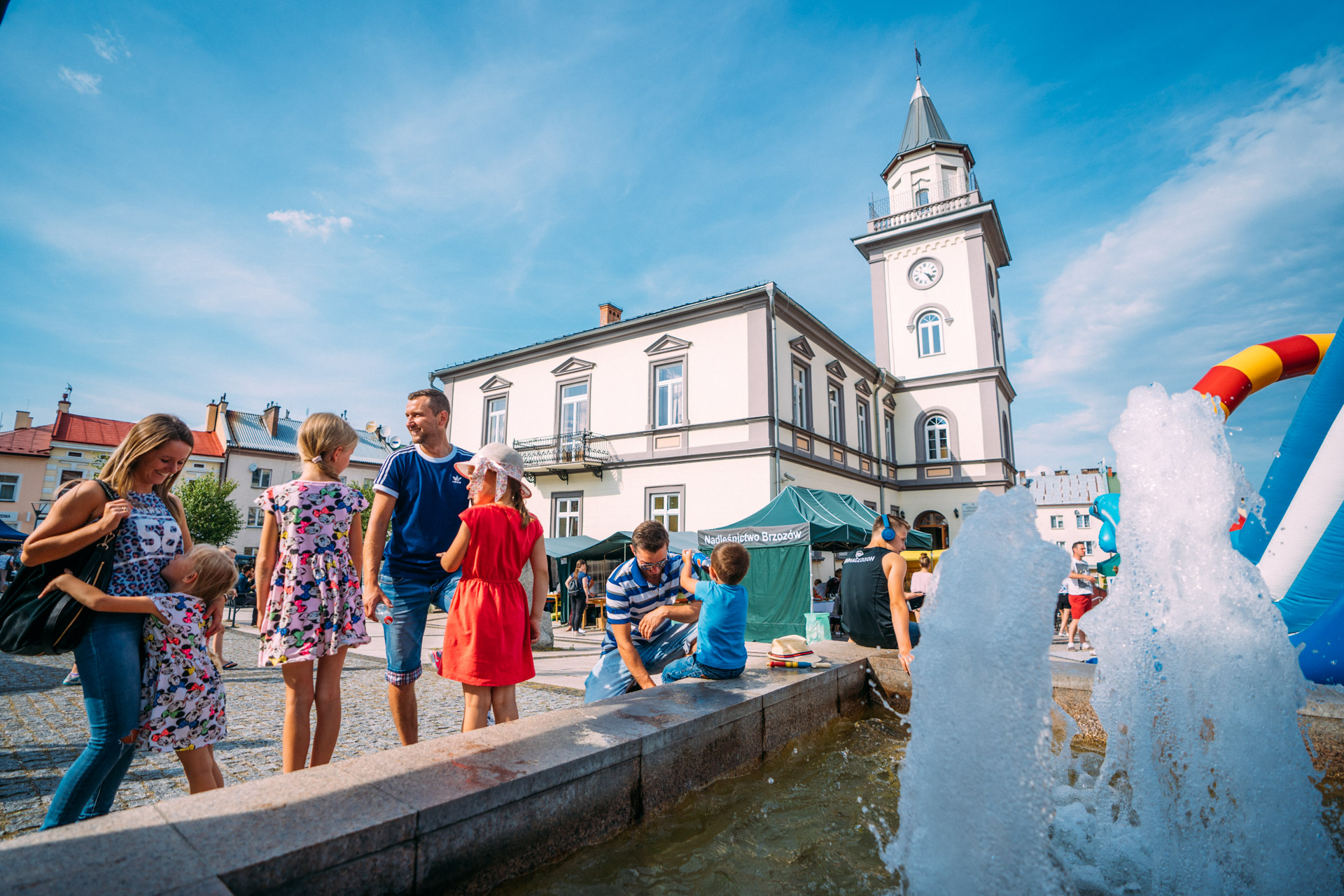 Kobieta i mężczyzna z trzema dziewczynka stoją przy fontannie. W głębi ratusz