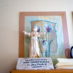 Mała rzeźba przedstawiająca Jana Pawłą II. Za rzeźbą obrazy w ramkach