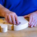 Osoba w niebieskim t-shircie gładzi papierem ściernym kwiat z drewna