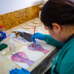 Kobieta w ciemnych włosach i w zielonym kitlu maluje anioły