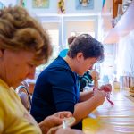 Kobiety siedzą przy stole i ucinają nitki nozyczkami