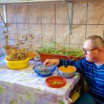 Mężczyzna w swetrze w paski siedzi przy stole i dotyka nasiona, które znajduja się w misce