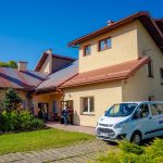 Parterowy budynek z poddaszem. Przed budynkiem biały bus osobowy