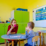Chłopiec siedzi przy stole podczas zajęć logopedycznych po opieką specjalistki