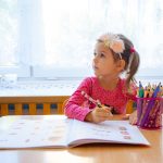 Dziewczynka z opaską na głowie wypełnia zadania w książce