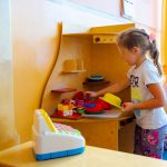 Dziewczynka bawi się dziecięca kuchnią z tyłu różowy wózek