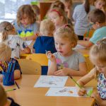 Dzieci siedzą przy stołach i rysują na kartkach
