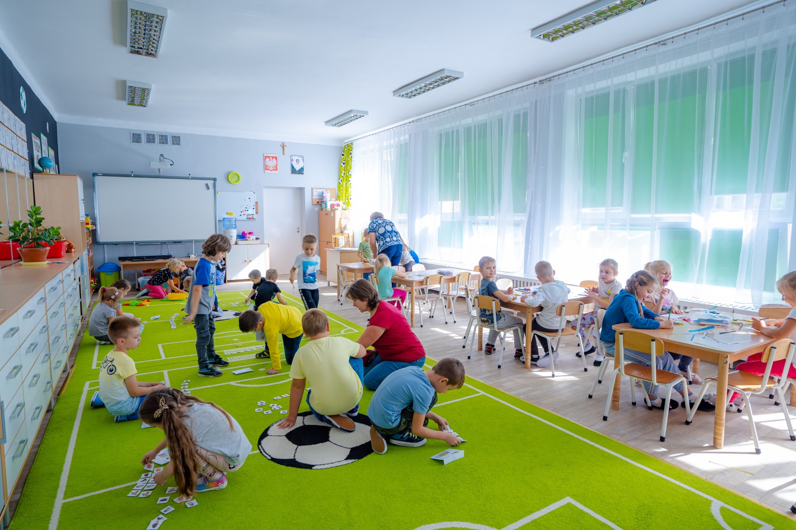 Dzieci bawią się na podłodze i rysuja przy stolikach