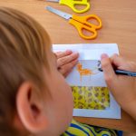 Chłopiec rysuje zwierzątko. Na stole leżą nożyczki