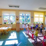 Kobieta w ciemnej bluzce tańczy. Przed nia grupa dzieci, która naśladuje jej ruchy