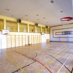 Duża sala gimnastyczna z jasnym parkietem. Na parkiecie wymalowane linie do gier zespołowych. Na