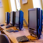 Wygaszone monitory koloru czarnego i klawiatury ustawione na biurkach. Przy biurkach fotele obrotowe