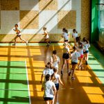 Dziewczyny w strojach gimnastycznych biegną w szeregu po sali gimnastycznej