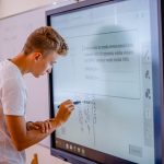 Chłopiec w białym t-shircie pisze na tablicy interaktywnej