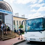 Młodzież wychodzi z białego autokaru i idzie po schodach do budynku pływalni