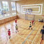 Mecz piłki ręcznej na sali sportowej. Piłkarze w strojach czerwonych i seledynowych