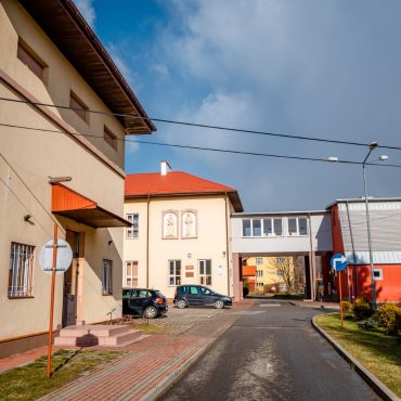Zzespół budynków połaczonych łącznikiem. Budynki po lewej stronie mają żółte elewacje, budynek po prawej czerwoną