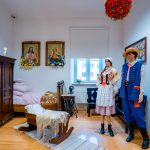 Pokój ze starymi, lecz dobrze utrzymanymi meblami. Na pierwszym planie kołyska i dwa manekiny w ludowych strojach