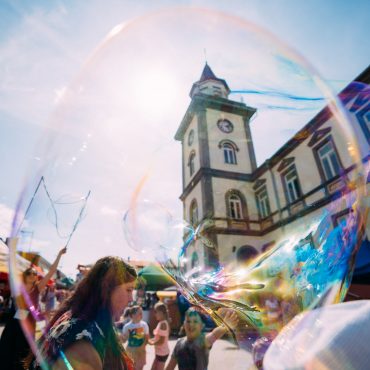 Młodzież puszcza wielkie bańki mydlane na placu przed ratuszem z wieżą