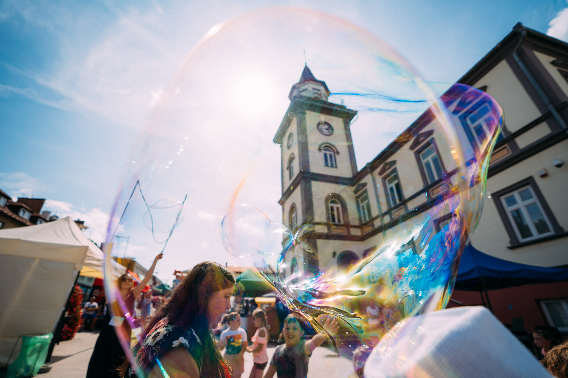 Młodzież puszcza wielkie bańki mydlane na placu przed ratuszem z wieżą