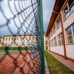 Dwukondygnacyjne budynki szkolne ze spadzistymi dachami. Przed budynkami boisko sportowe ze sztuczną nawierzchnią