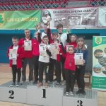 Grupa dzieci stoi na podium z pucharami w rękach