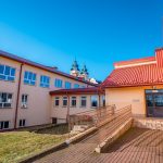 Trókondygnacyjny budynek szkolny z podjazdem dla osób niepełnosprawnych. W głebi barokowy kościół z dwoma wieżami