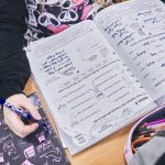 Zeszyt do języka angielskiego leży na stole. Widac rękę dziecka z długopisem w ręku