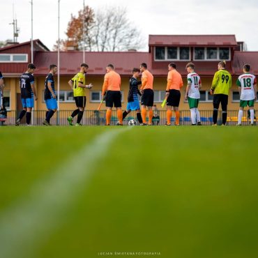 Grupa młodych piłkarzy na boisku. Stoją ustawieni w rzędzie.
