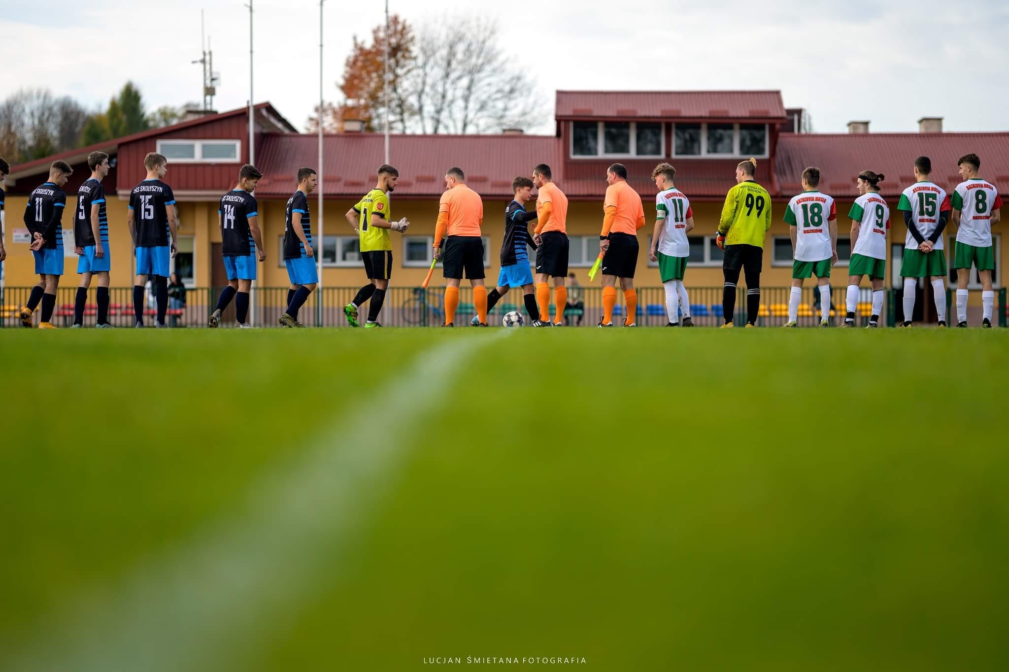 Grupa młodych piłkarzy na boisku. Stoją ustawieni w rzędzie.