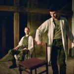 Dwóch mężczyzn w białych kitlach. Jeden z nich siedzi na krześle, a drugi przenosi krzesło