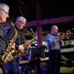 Trzech siwych mężczyzn gra na instrumentach muzycznych - dwóch na saksofonach, a trzeci na puzonie