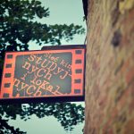 Czerwono-czarny szyld z napisem "Sieć kin studyjnych" zawieszony na ceglanym murze