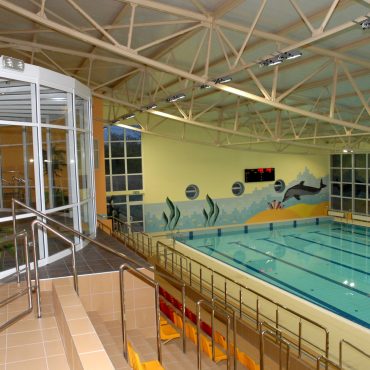 Kryty basen pływacki z trybunami dla widzóa. Na ścianiekolorowe malunki