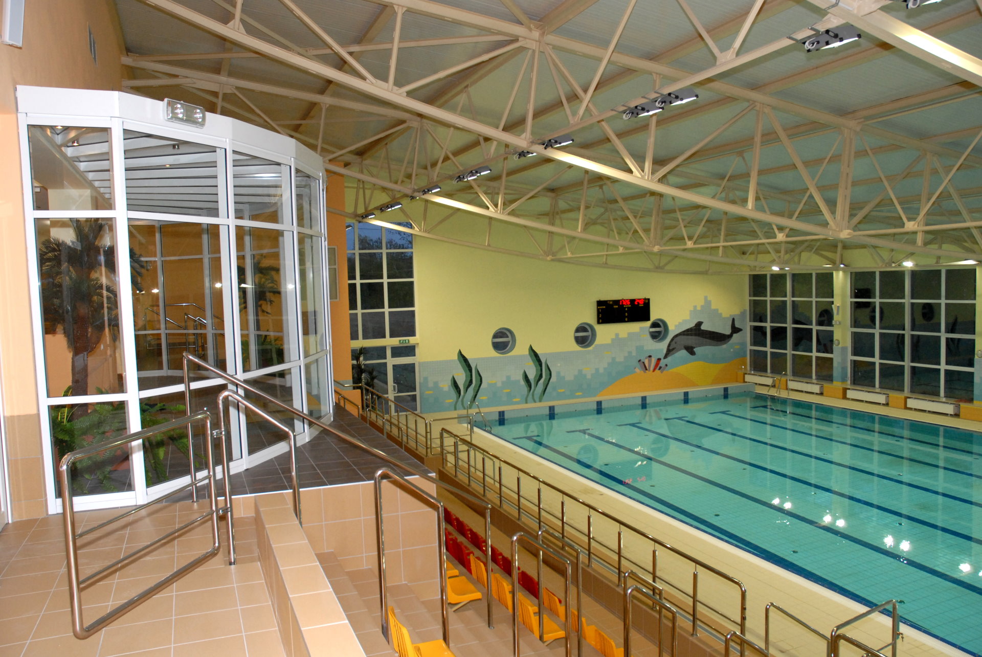 Kryty basen pływacki z trybunami dla widzóa. Na ścianiekolorowe malunki