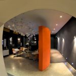 W nowoczesnym wnętrzu okragłe stoliki z drewnianymi krzesłami. Sciany pomalowane na brązowo i pomarańczowo. Pod sufitem dużo lamp z okragłymi kloszami