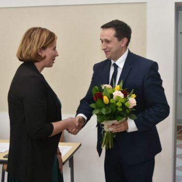 Mężczyzna w garniturze przekazuje bukiet kwiatów kobiecie o krótkich włosach.