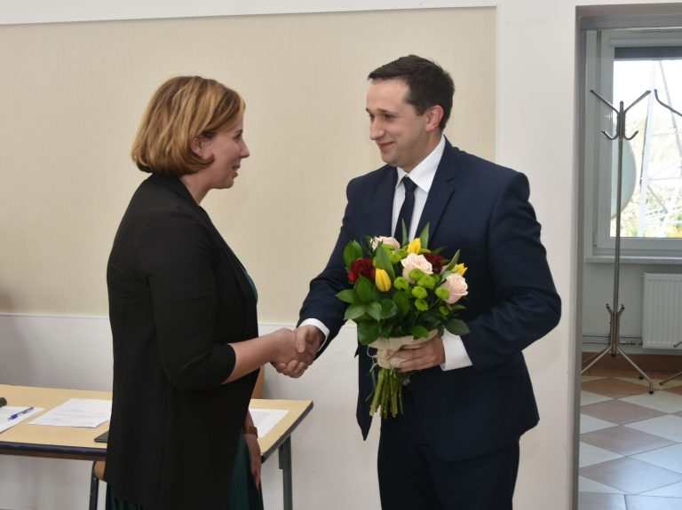 Mężczyzna w garniturze przekazuje bukiet kwiatów kobiecie o krótkich włosach.