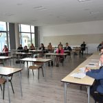 Grupa osób w tym mężczyzn i kobiet słuchają wideokonferencji.