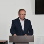 Mężczyzna w średnim wieku przemawia do zgromadzonych.