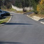 Ulica z nową nawierzchnia asfaltową u wyraźnymi krawężnikami. Po lewej stronie stoi biały bus, a za no samochód osoboy.