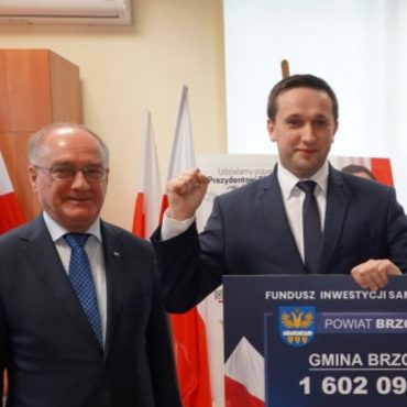 Młody mężczyzna cw granatowym garniturze i granatowym krawacieieszy się z otrzymania pieniędzy.