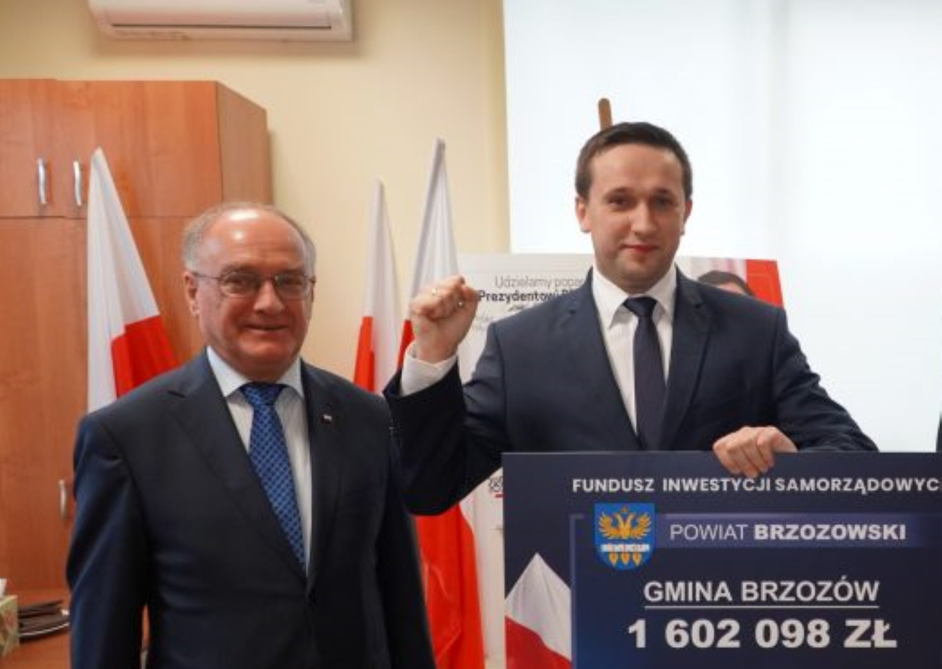 Młody mężczyzna cw granatowym garniturze i granatowym krawacieieszy się z otrzymania pieniędzy.