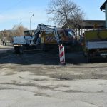 Zniszczona droga, dziurawa. Koparka wykopuje ziemię.