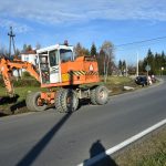 Pomarańczowa koparka wykopuje ziemię przy głównej ulicy.