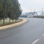 Widok na drogę asfaltową, przy której znajduje się chodnik z kostki brukowej.