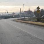 Widok na drogę asfaltową, przy której znajduje się chodnik z kostki brukowej.