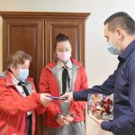 Młody mężczyzna w koszuli częstuje czekoladą i cukierkami dwie kobiety ubrane z mundury harcerskie.