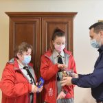 Młody mężczyzna w koszuli częstuje dziewczynę cukierkami, które znajdują się w miseczce szklanej.