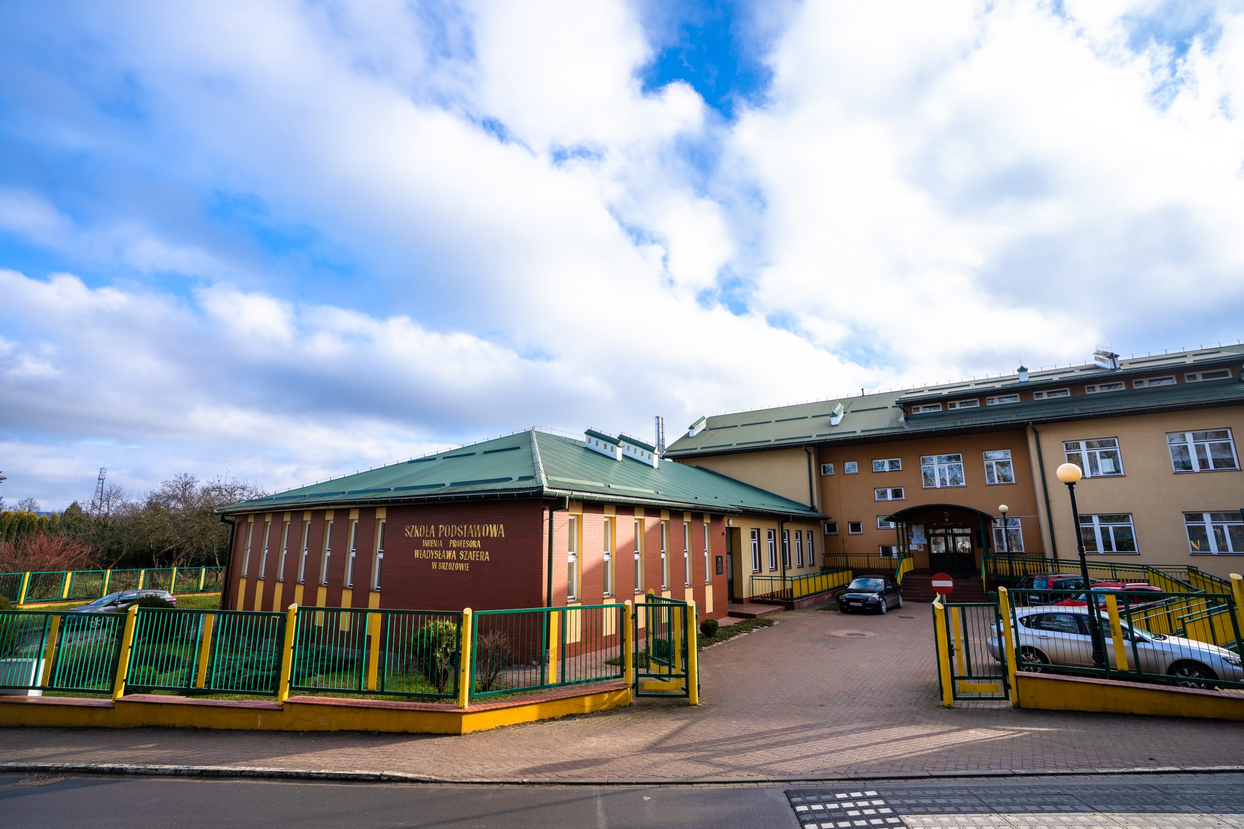 Duży, piętrowy budynek szkoły, znajdujący się przy głównej ulicy otoczony bramą.